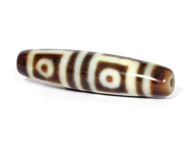 V-070226-4E dzi bead, full-length diagonal view, dark brown motif on cream ground, unretouched.