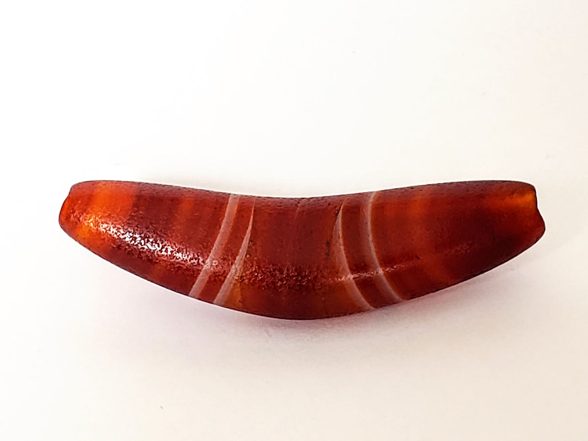 Bow-shaped natural banded agate dzi bead with red-orange striping and polished surface on white background
