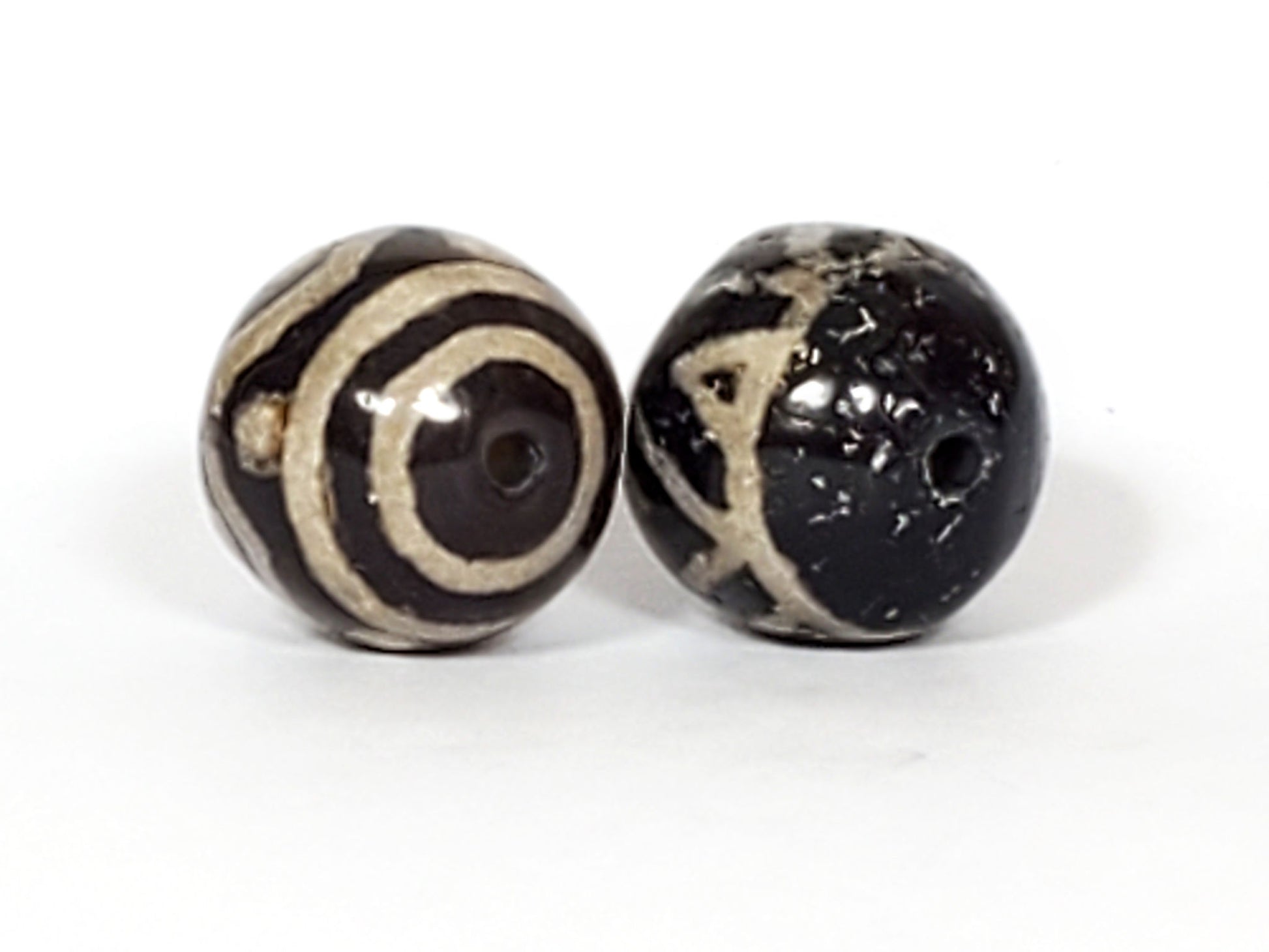 V-FA-062526-TSWS-TT pair round agate dzi, drilling view, Bead A eye motif visible, Bead B wave tooth pattern, unretouched