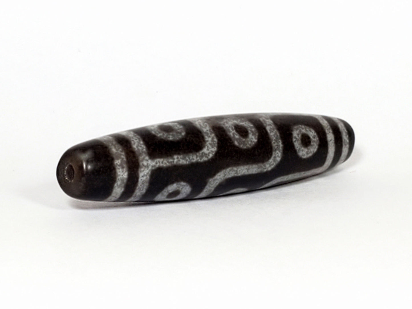 N-062226-9E, angled view toward broader end, drill hole centred, flowing curved motif visible, grey-black, unretouched