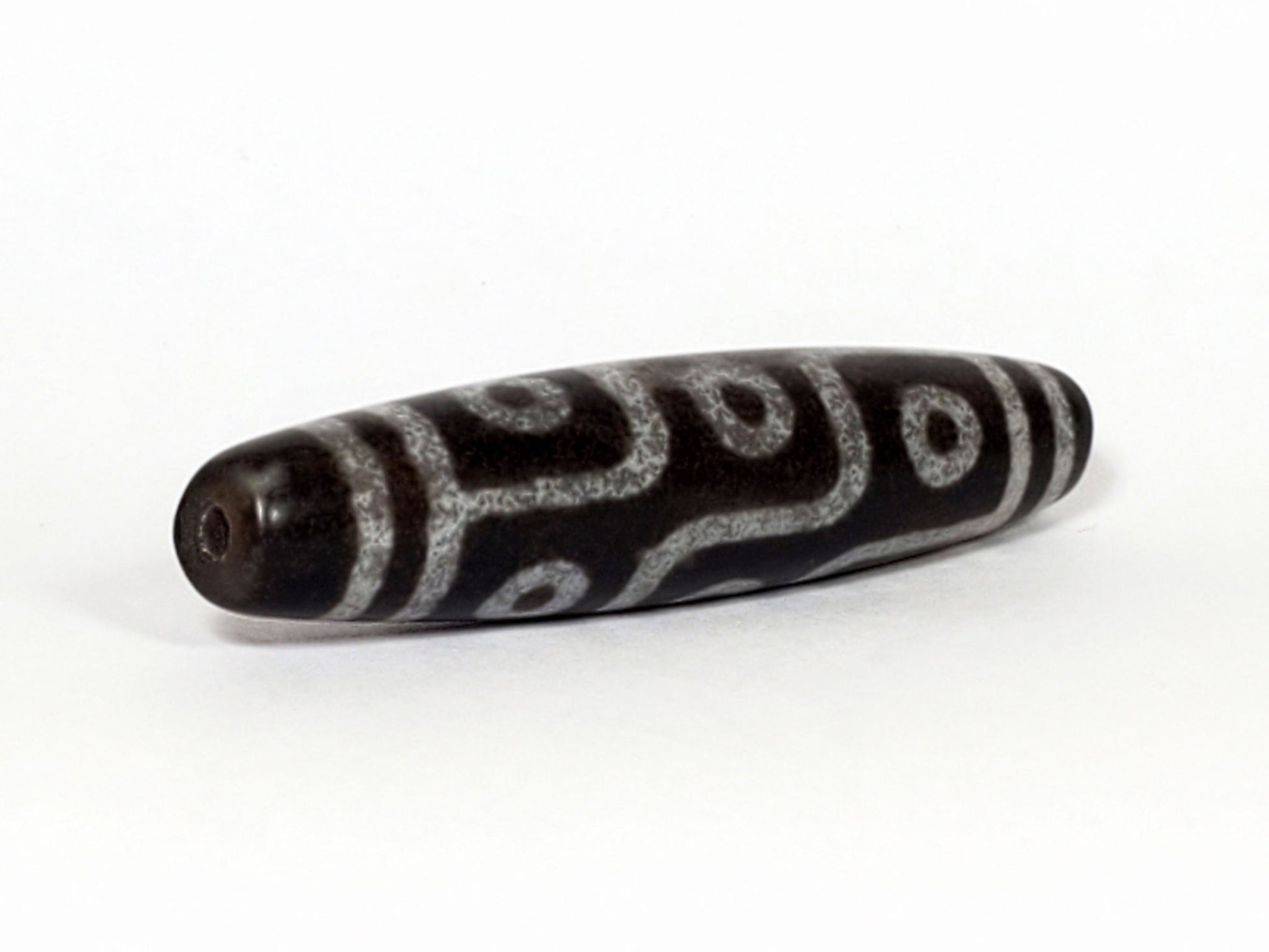 N-062226-9E, angled view toward broader end, drill hole centred, flowing curved motif visible, grey-black, unretouched