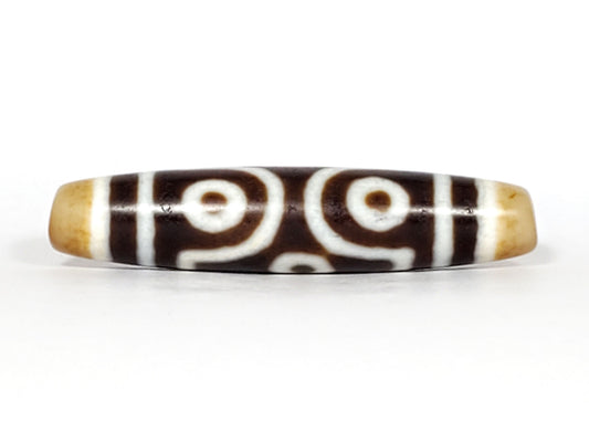 Face D, diamond frame single eye): Face D of antique six eye dzi At-053026-6E, single eye within diamond compass-rose frame on deep brown agate, honey-gold end caps, 54.9mm × 12.3mm, unretouched