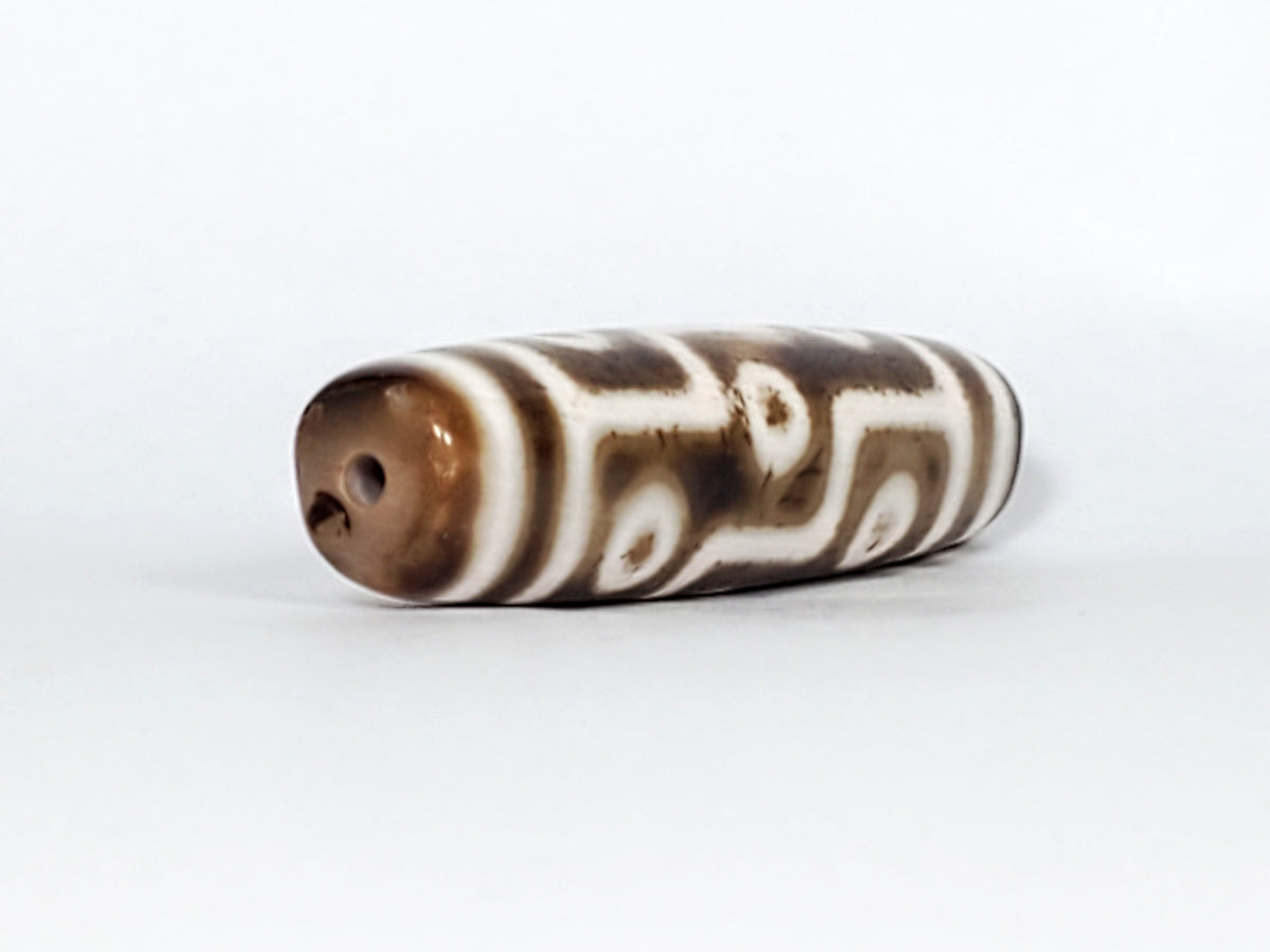 Antique Qing Dynasty nine-eye dzi bead, brown agate with white wave motifs, visible drill hole and natural patina