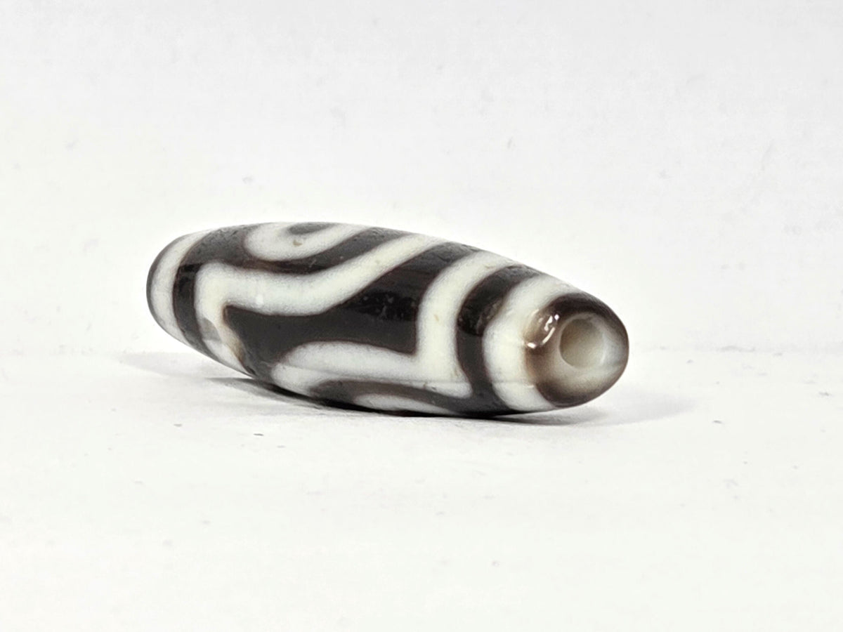 End cap view of antique two eye dzi bead At-010726-2E3, dark brown agate tip, drill hole centred, torpedo body tapering, near-black agate, 38.6mm