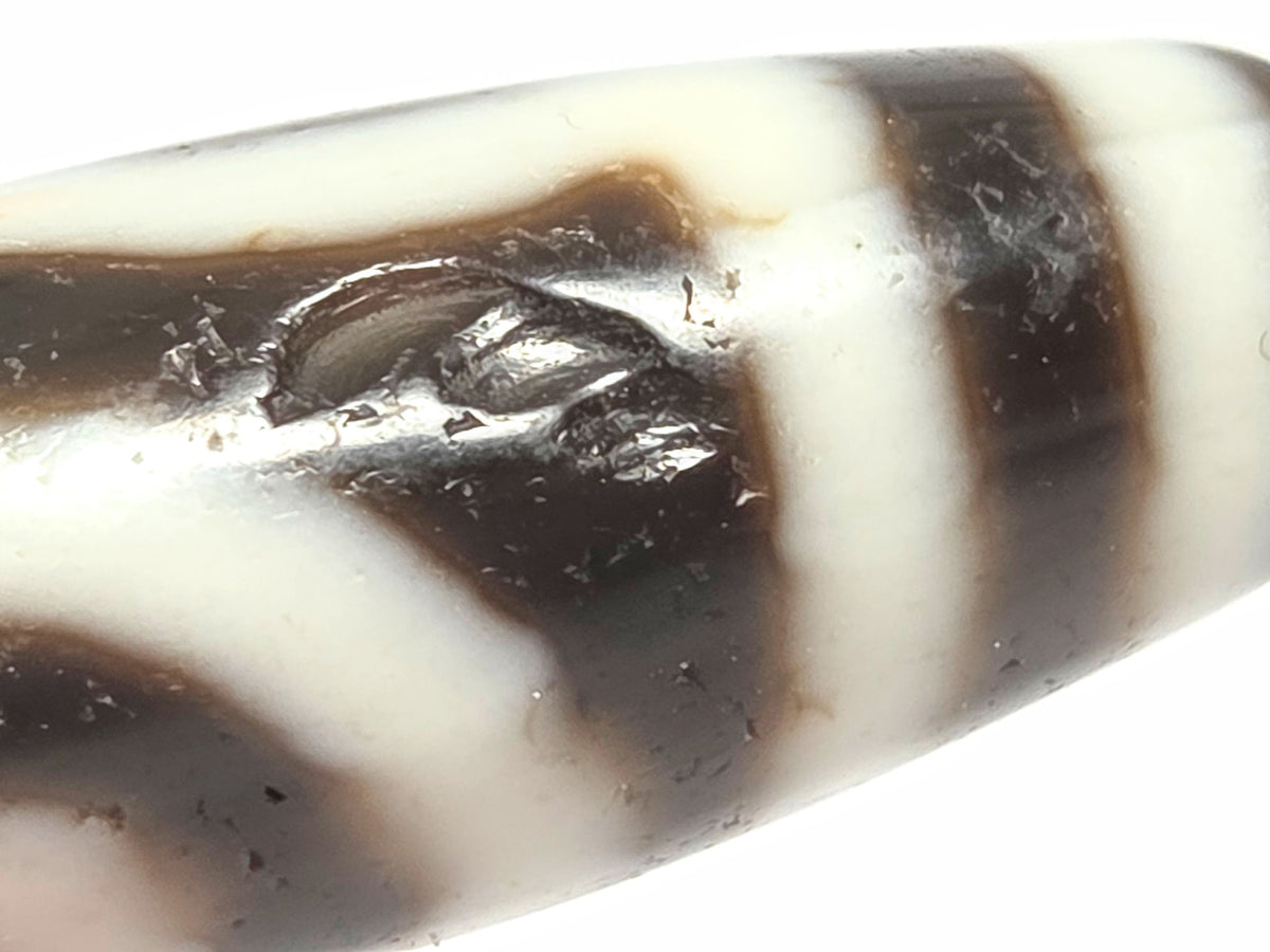 Another close detail of antique two eye dzi bead At-010726-2E3 showing medicine dig on near-black agate surface, authentic age marking, unretouched photography