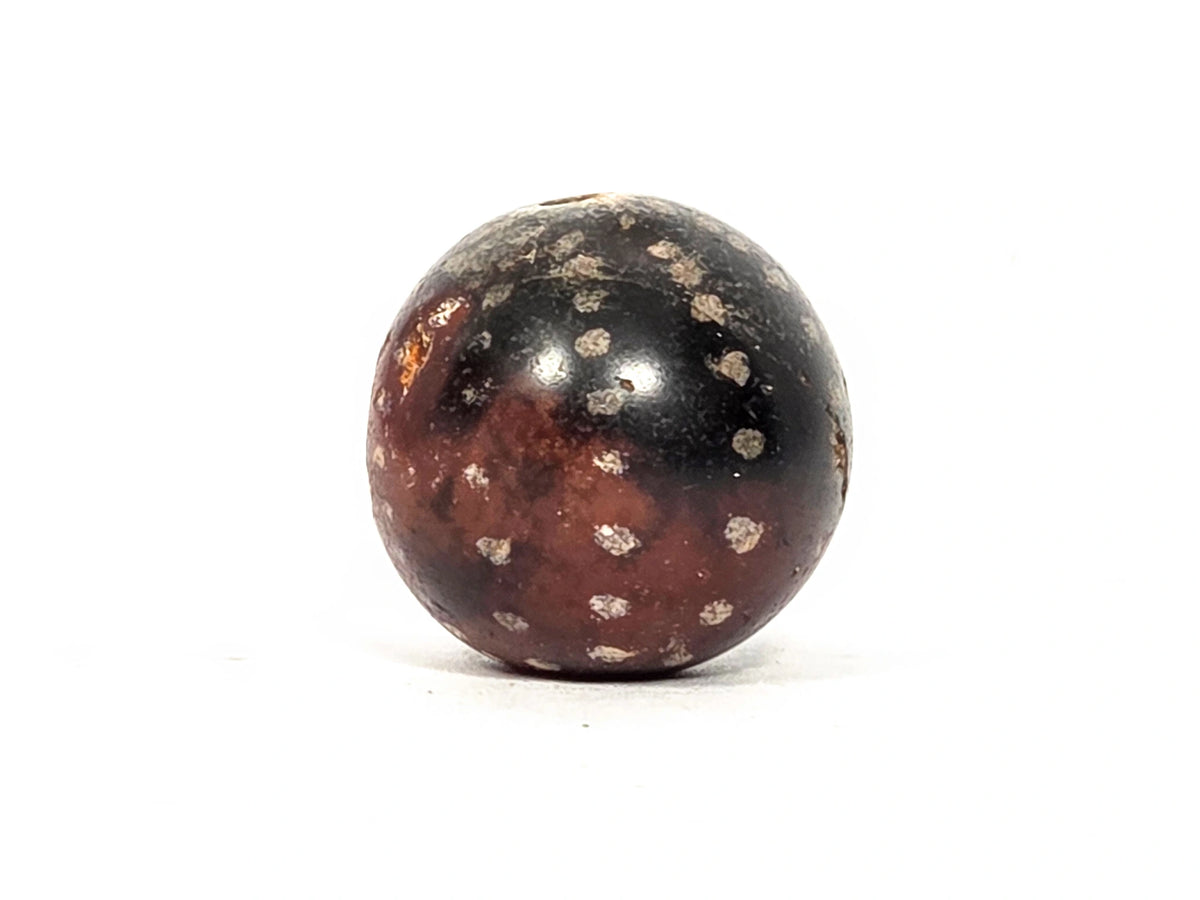 Ancient round agate bead AC-101126-RS, first profile view showing near-spherical form with scattered cream-silver mineral star inclusions across deep dark brown agate surface, 1500–2000 years old