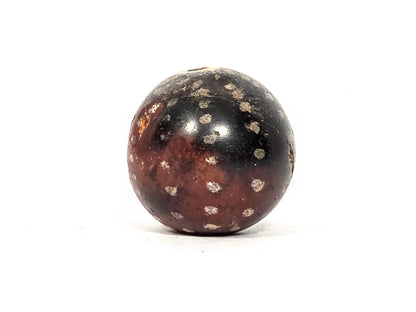 Ancient round agate bead AC-101126-RS, first profile view showing near-spherical form with scattered cream-silver mineral star inclusions across deep dark brown agate surface, 1500–2000 years old