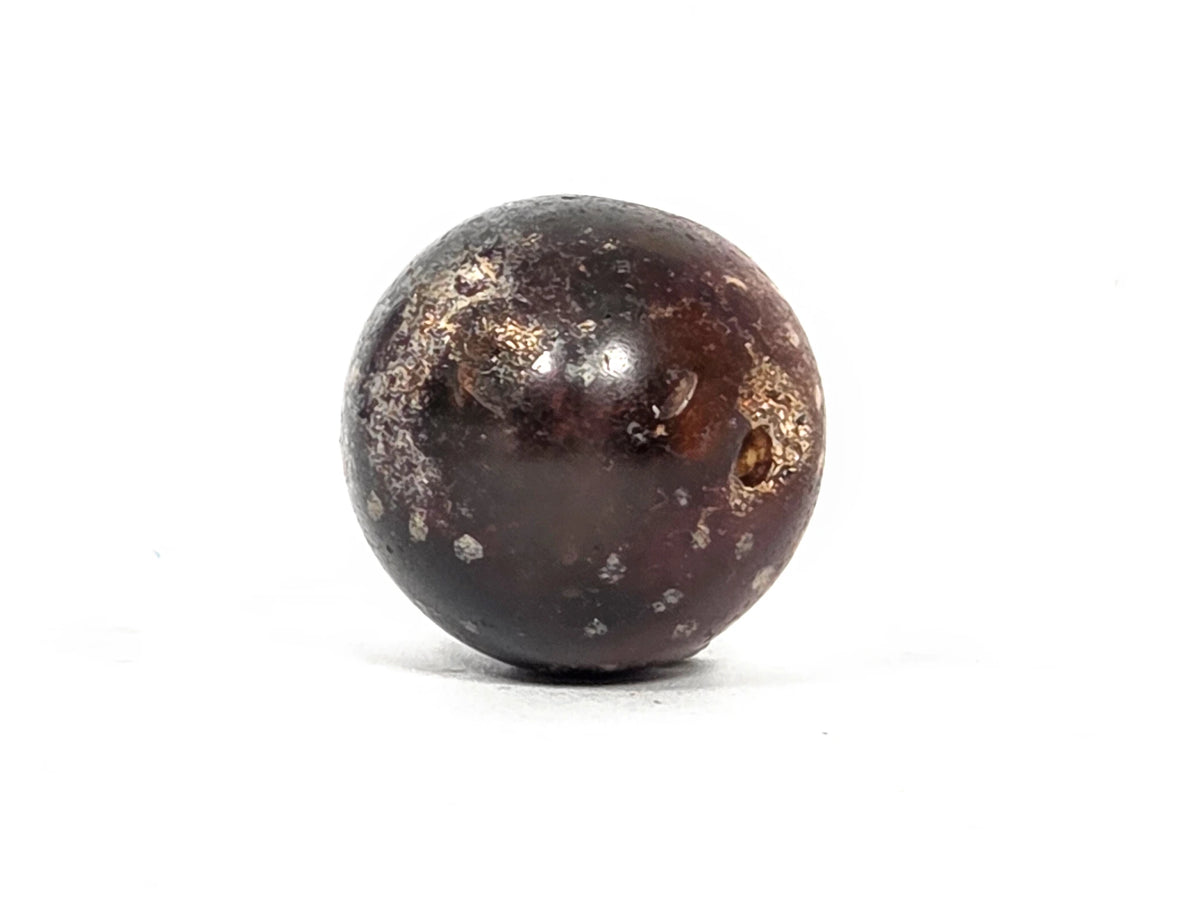 End view of ancient round agate bead showing drill hole aperture with cream-tan calcification deposits surrounding the opening in the dark brown agate tip, 1500–2000 years old