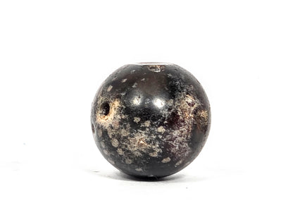 Opposite end view of ancient round agate bead AC-101126-RS showing second drill hole in deep charcoal-grey hemisphere with extensive cream-grey calcification spreading broadly around the aperture, 1500–2000 years old