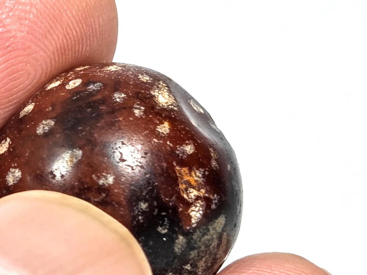 Fifth profile view of ancient round agate bead AC-101126-RS showing equatorial zone with scattered cream-silver mineral inclusions and the dimple surface defect visible in the agate body