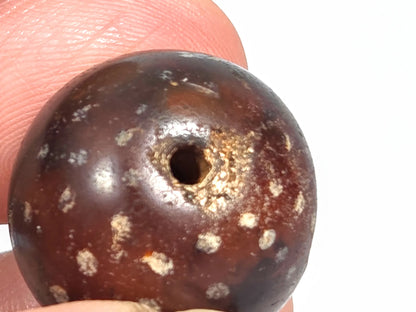 Macro close-up of ancient round agate bead showing natural dimple depression defect in the stone surface, scattered mineral star inclusions, and aged agate texture, 1500–2000 years old
