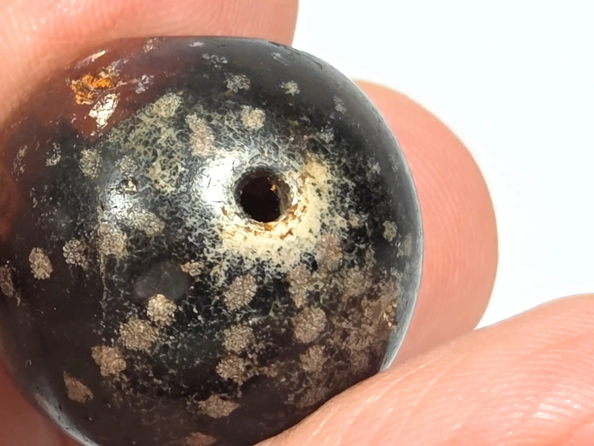 Wide macro view of ancient round agate bead AC-101126-RS showing distribution of cream-silver mineral star inclusions across dark brown agate surface and natural stone character