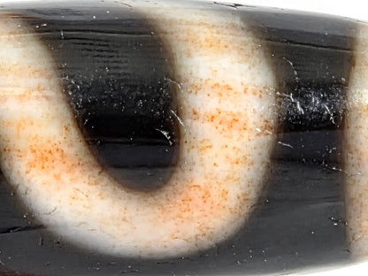 Macro detail of antique money hook dzi bead showing bloodspot patina — rich warm amber to rust-orange iron mineral staining concentrated through cream-white motif zones, with surface texture of aged agate visible, 100–300 years old