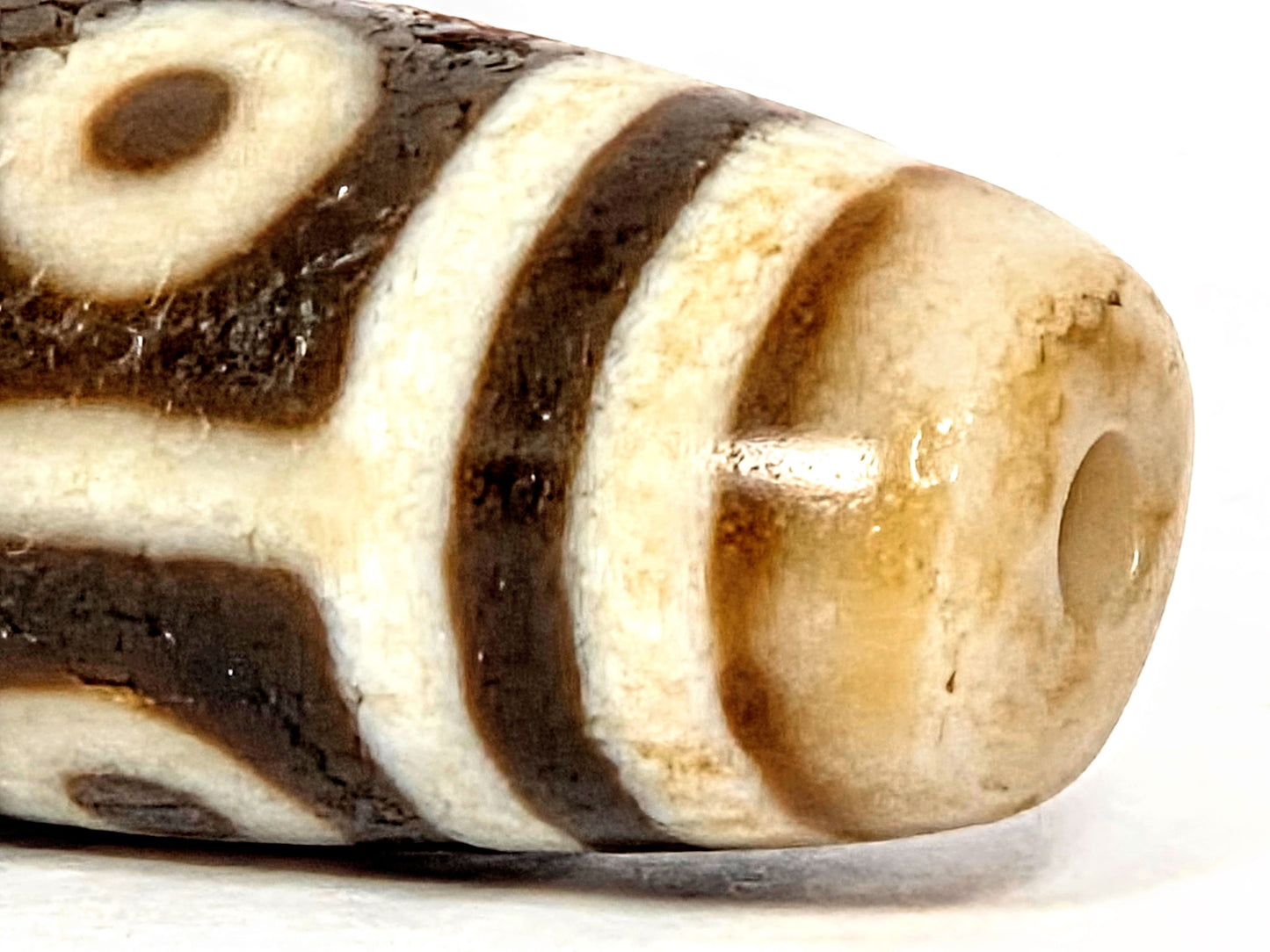 End close-up of ancient Nine Eye Dzi bead — warm amber agate visible at drill hole, natural patina and surface character of ~800 year old white agate