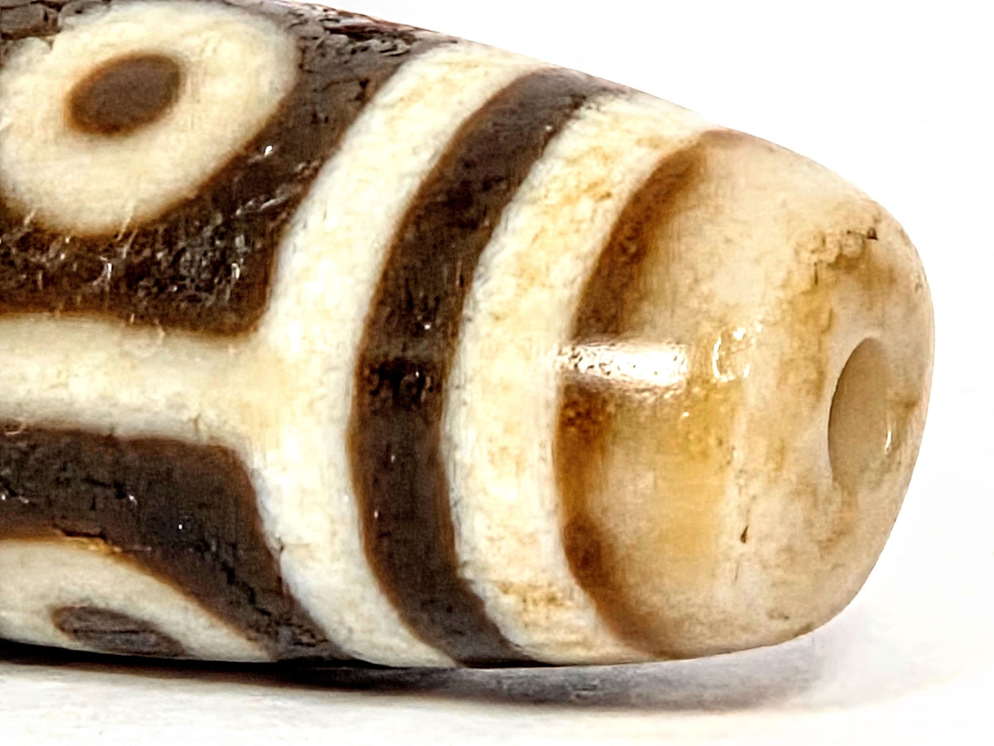 End close-up of ancient Nine Eye Dzi bead — warm amber agate visible at drill hole, natural patina and surface character of ~800 year old white agate