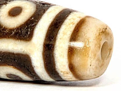 End close-up of ancient Nine Eye Dzi bead — warm amber agate visible at drill hole, natural patina and surface character of ~800 year old white agate