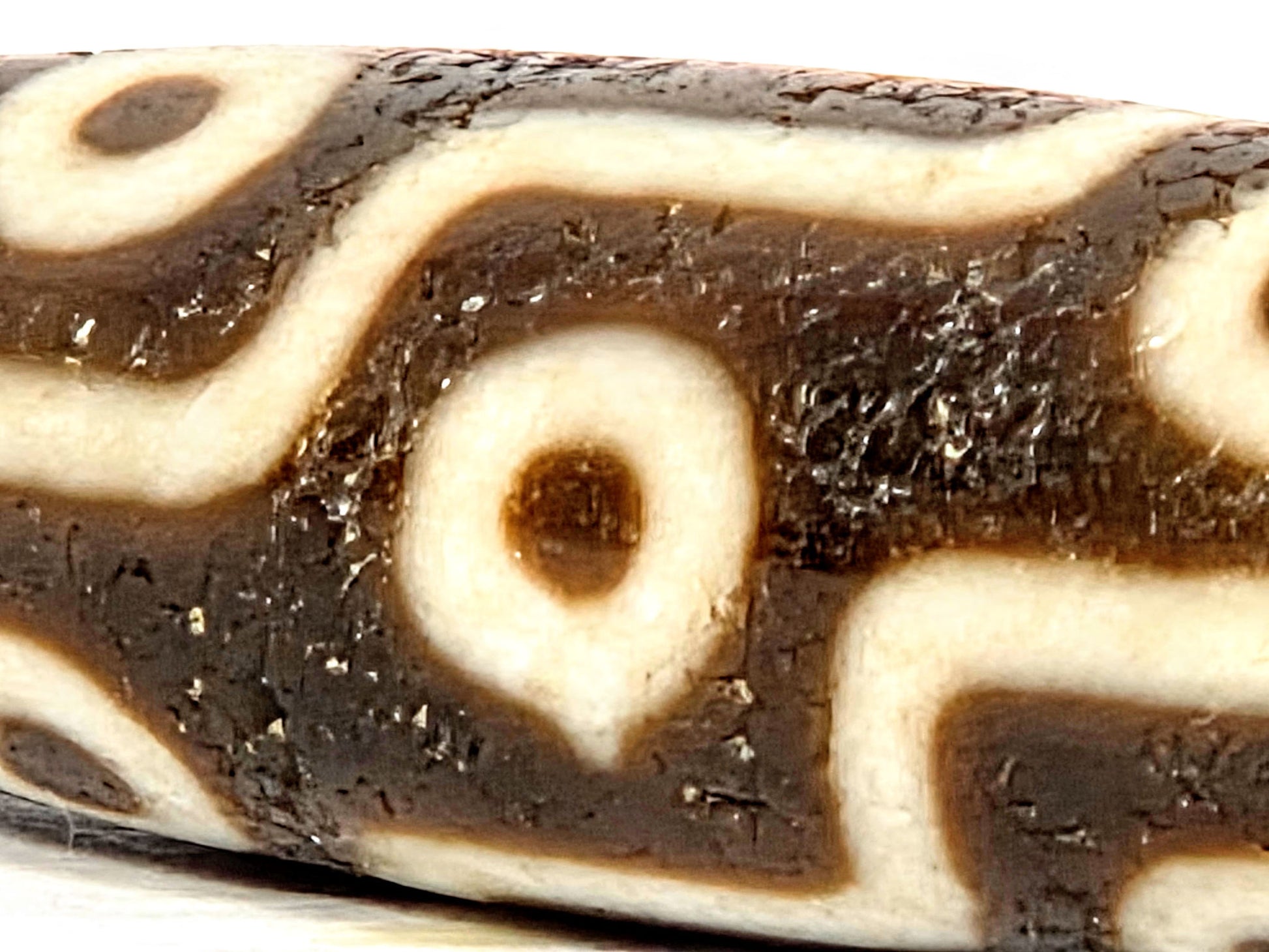 Macro close-up of eye circle motif on ancient Nine Eye Dzi bead — warm amber-honey white agate with deep etching, 800 year old Tibetan craftsmanship