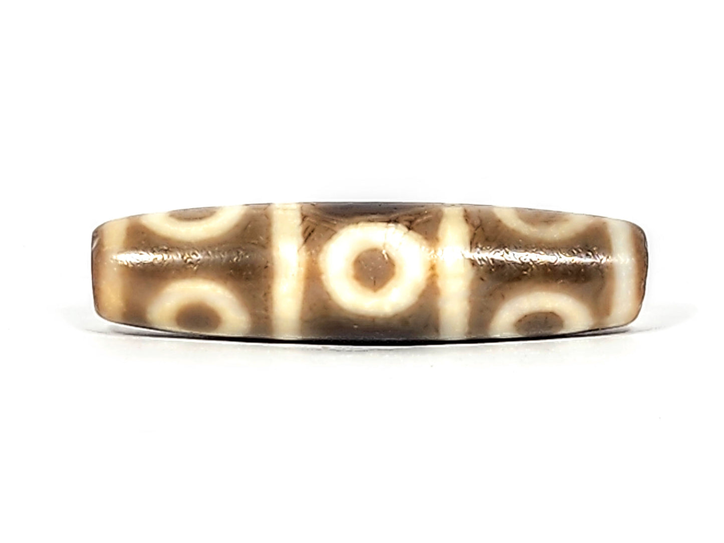 Third face of ancient Eight Eye Dzi — five eye circles visible, crisp cream rings, warm brown agate