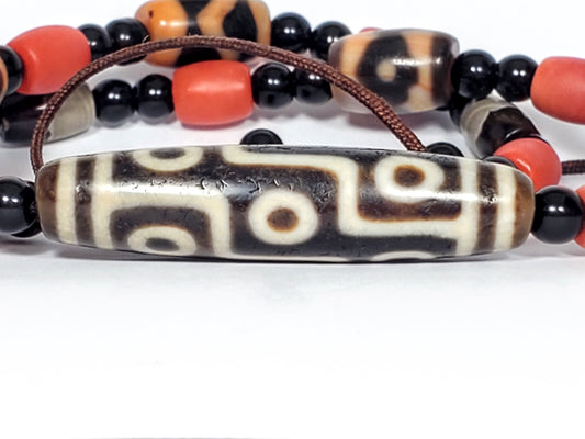 Ancient Tibetan nine-eye dzi bead, dark agate with cream eye motifs, aged patina, weathered surface texture, elongated barrel shape
