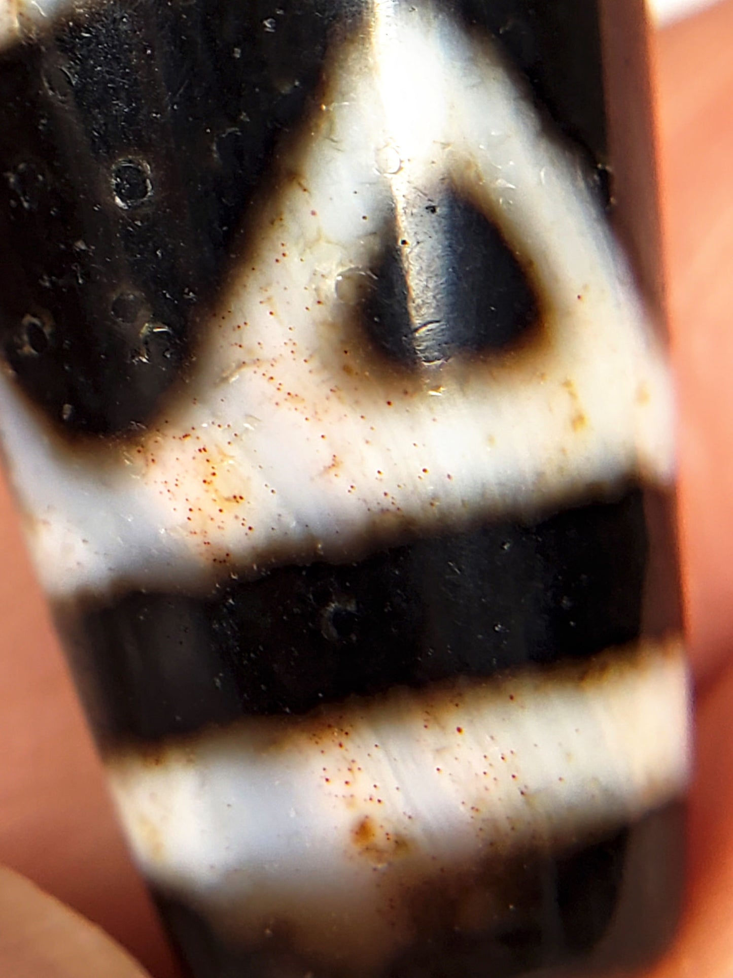 Close-up of tiger tooth etching on ancient Tibetan Dzi bead — triangular pattern and agate surface texture with cinnabar staining visible, unretouched