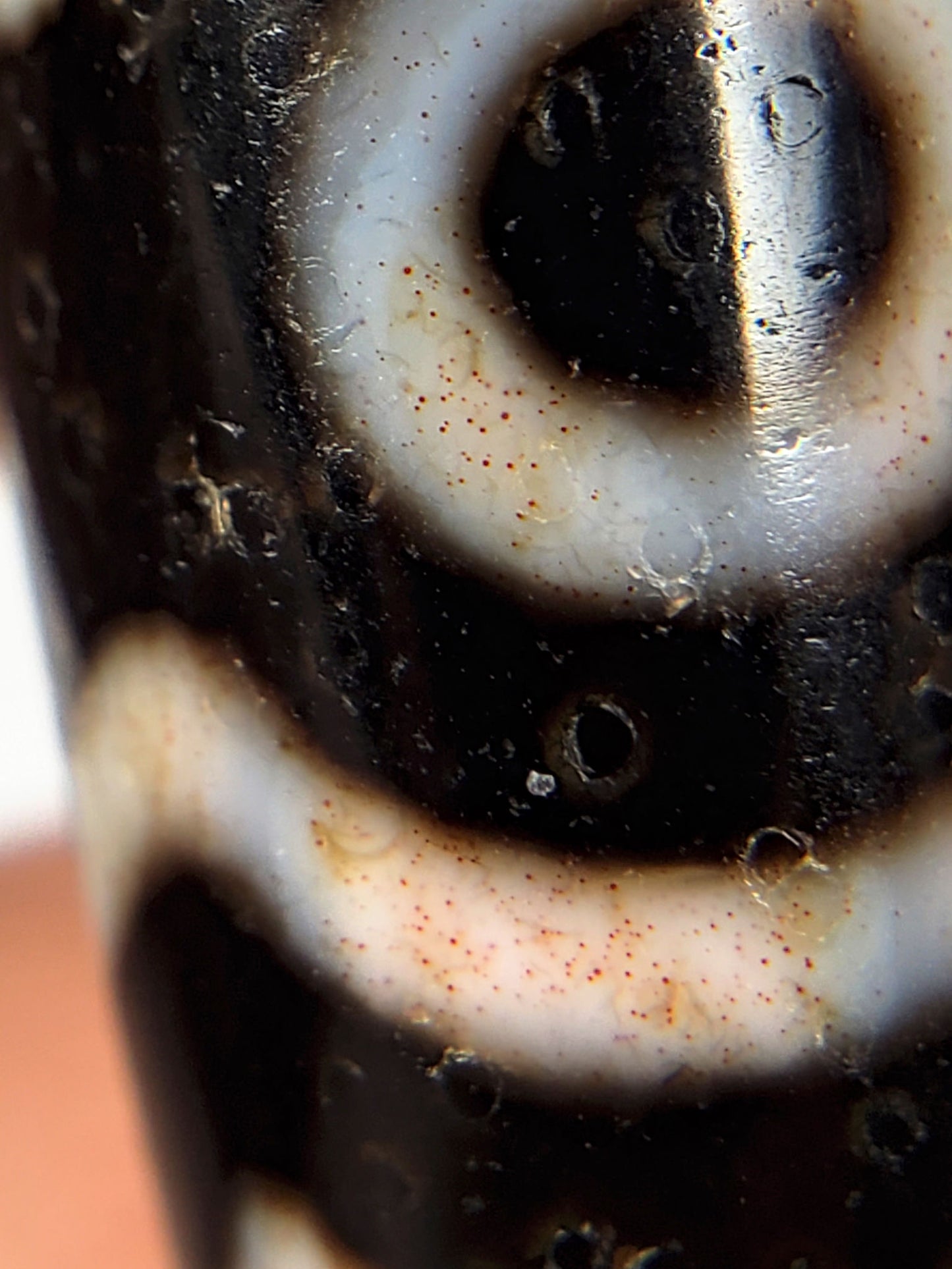 Close-up of eye motif etching on ancient Three Eye Dzi bead — cream circle on deep black natural agate, 500+ years old, genuine Tibetan amulet