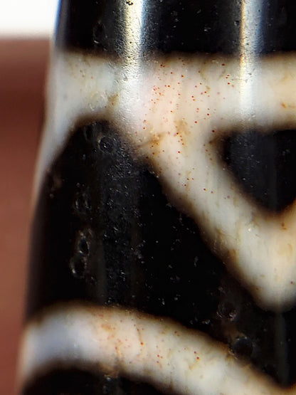 Extreme macro of cinnabar bloodspot on ancient Tibetan Dzi bead — deep red vermillion mercuric sulfide inclusion visible in natural agate, unretouched