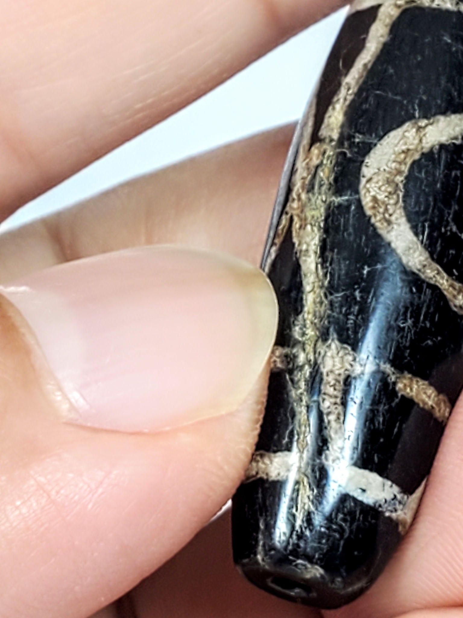 Another hand-held view of ancient Tibetan Two Eye Dzi bead showing calcification depth and surface character