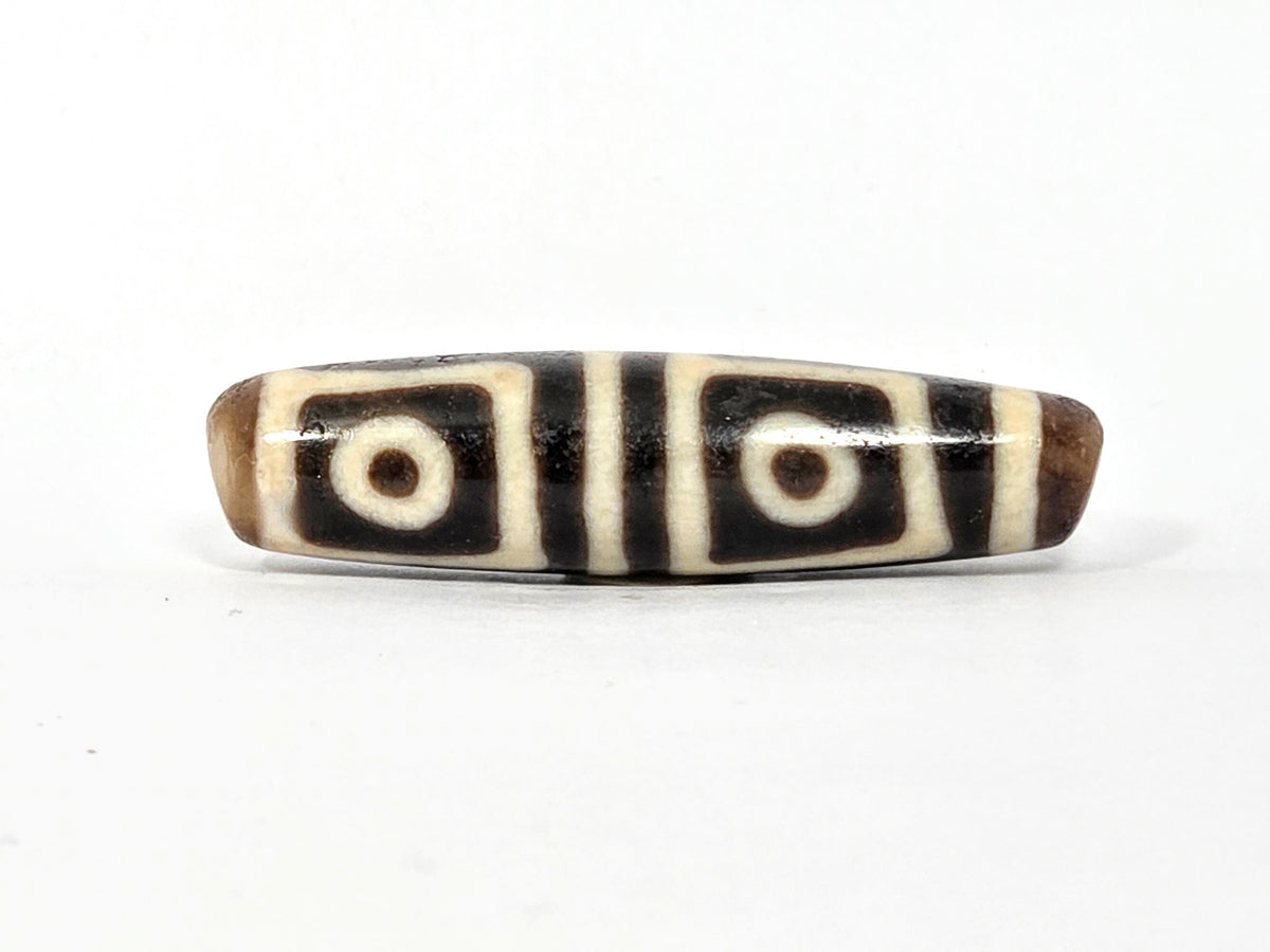 Four-eye dzi bead, square-framed eye motifs, deep warm brown agate, cream stripes, smooth patina, 49.5mm elongated barrel shape
