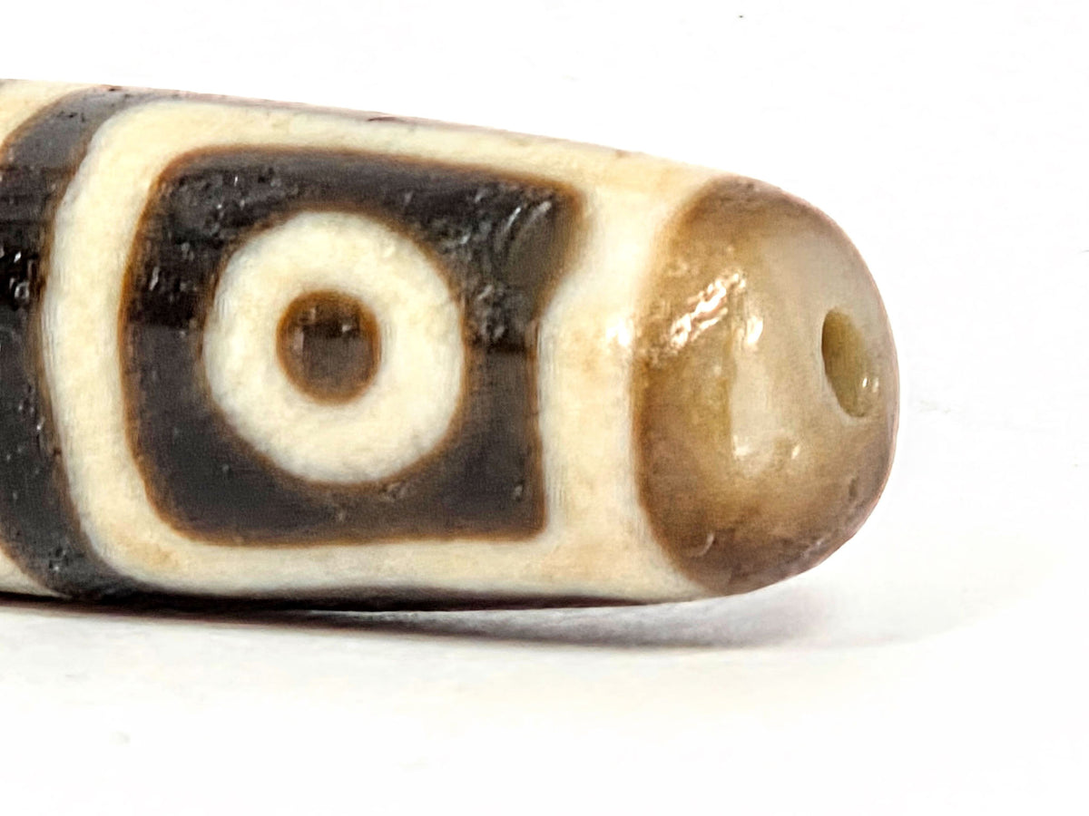 Four-eye dzi bead with square-framed eye motifs, deep warm brown agate, visible drill hole, aged patina, 49.5mm barrel shape
