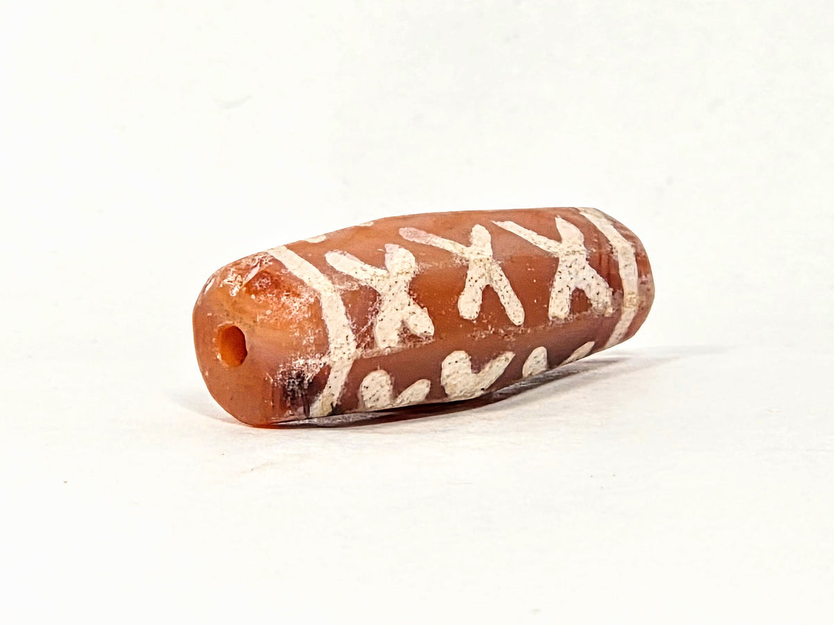 Ac-062426-12X ancient twelve X-cross carnelian dzi 28.5x11.0mm angled view drill hole end orange-red tip unretouched