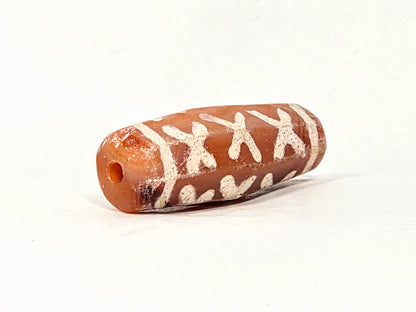 Ac-062426-12X ancient twelve X-cross carnelian dzi 28.5x11.0mm angled view drill hole end orange-red tip unretouched