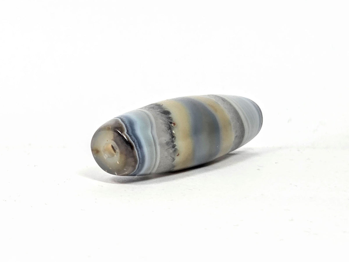 Antique one-eye Dzi bead, striped grey-blue agate, natural patina, visible drill hole, earthy tan banding, matte surface texture