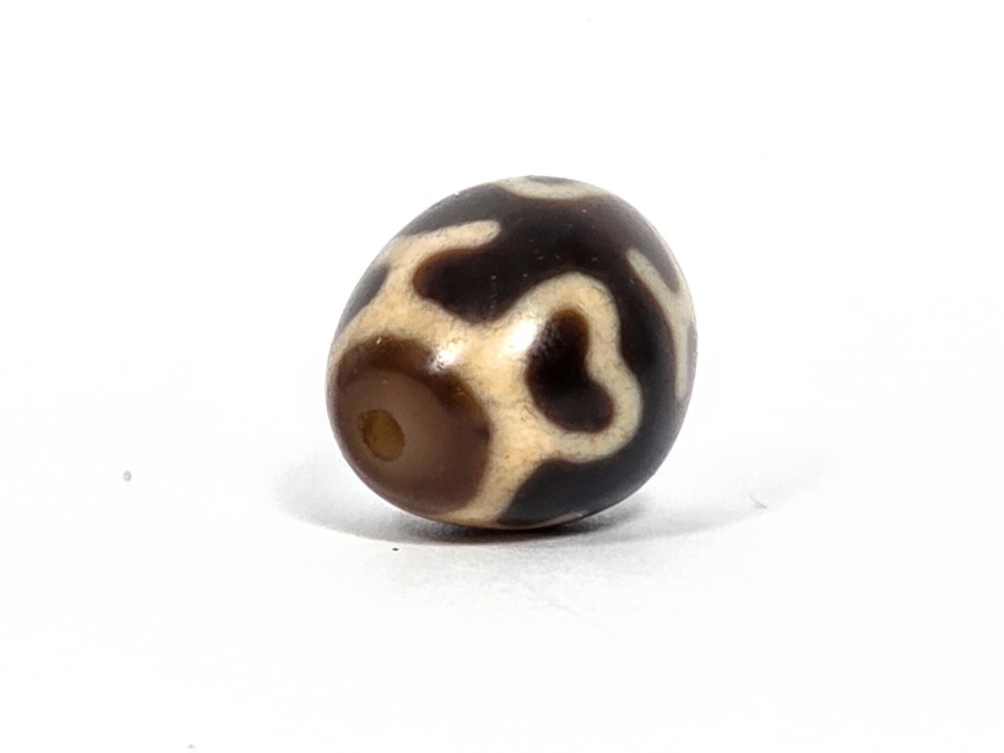 At-080926-4ELT antique round dzi bead 19.9×16.6mm, rotation F showing cream heart-lotus form and drill hole at lower left, unretouched