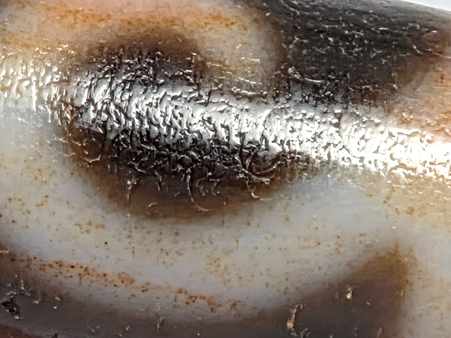 At-080426-GTBS2 macro motif scroll zone showing boundary-concentrated cinnabar bloodspots at cream-dark edges and age-crystalline texture throughout, unretouched