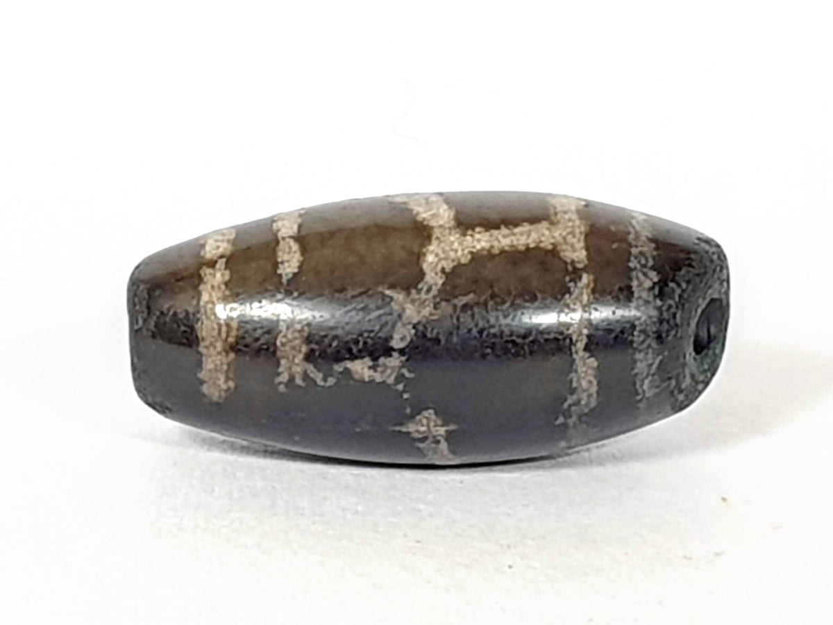 Antique Tibetan dzi bead longevity motif, dark agate, etched white grid pattern, visible drill hole, aged patina surface
