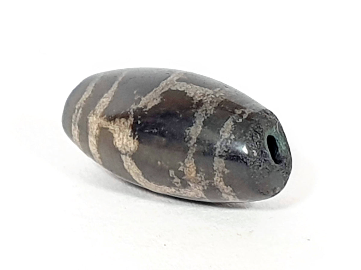Antique longevity motif dzi bead, dark agate with cream wave lines, aged patina, visible drill hole, brown bloodspots