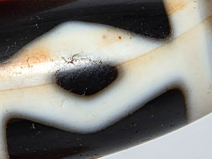 At-062126-6DE dzi bead, macro view of golden-brown accent banding and cinnabar, unretouched