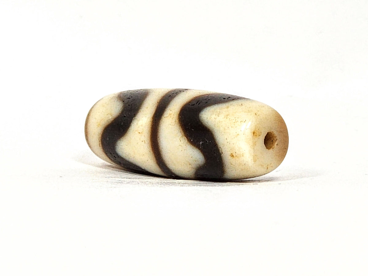 Opposite angle of antique Double Wave dzi At-072325-DW5, warm brown agate, cream wave S-curves, natural weathering marks on surface, compact torpedo profile, unretouched