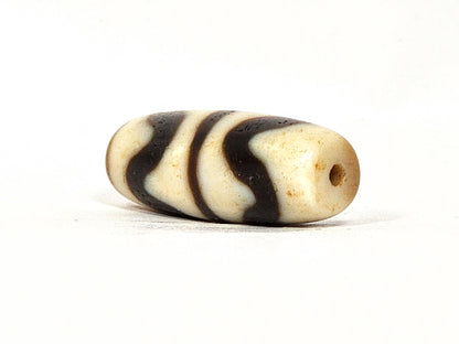 Opposite angle of antique Double Wave dzi At-072325-DW5, warm brown agate, cream wave S-curves, natural weathering marks on surface, compact torpedo profile, unretouched