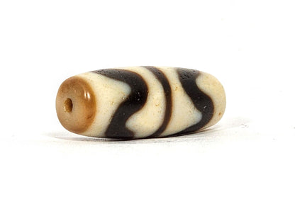 Three-quarter view of antique Double Wave dzi At-072325-DW5, warm brown end cap with drill hole, wave motif visible on compact torpedo body, 28.4mm × 10.6mm, unretouched