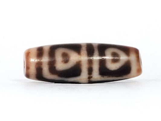 Three-quarter view of antique Four Leaf Bodhi dzi bead At-101624-FLB, compact barrel body, warm amber-brown agate, four arch-leaf motif, natural weathering marks, unretouched