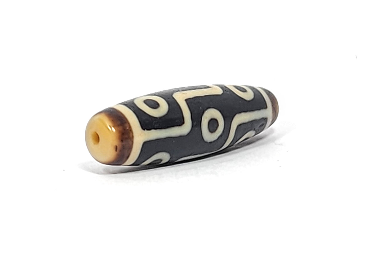 Antique Tibetan nine-eye dzi bead, black agate with cream white eye motifs, visible drill hole, aged patina, elongated barrel shape