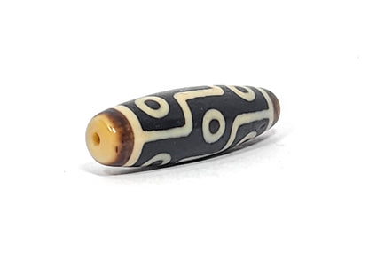 Antique Tibetan nine-eye dzi bead, black agate with cream white eye motifs, visible drill hole, aged patina, elongated barrel shape