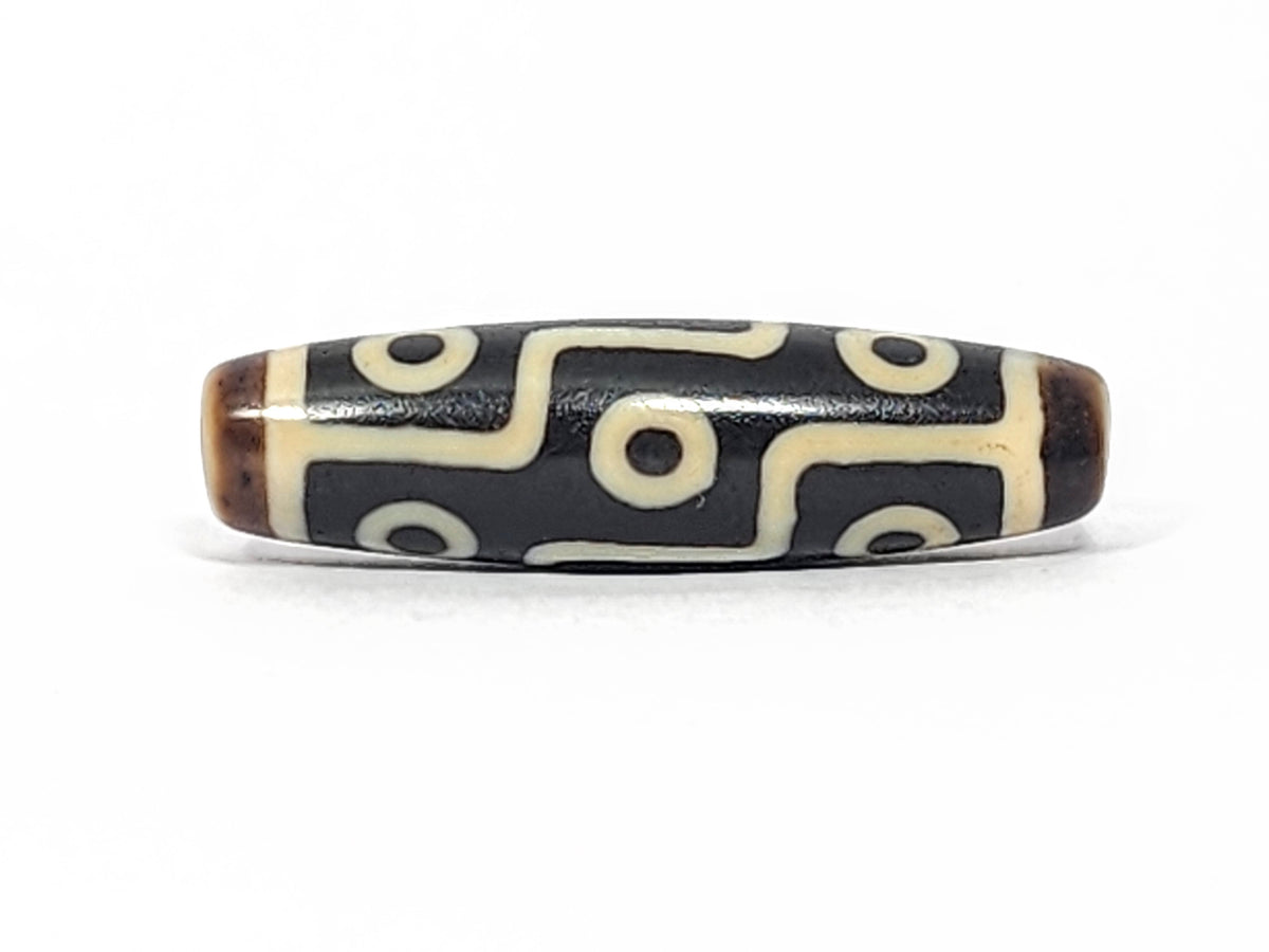 Antique Tibetan nine-eye dzi bead, black agate with cream white eye motifs and zigzag lines, brown patina on ends