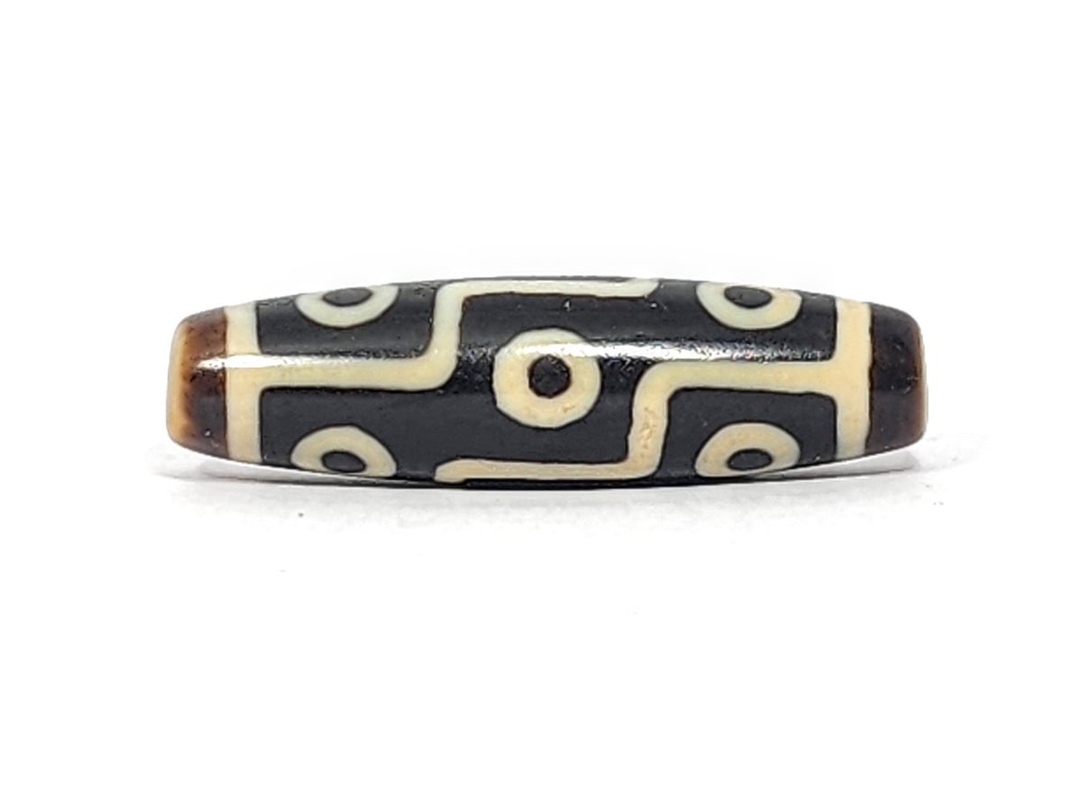 Antique Tibetan nine-eye dzi bead, dark agate with white eye motifs and wave lines, brown patina, elongated barrel shape