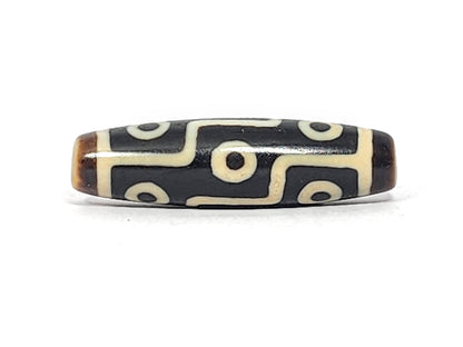 Antique Tibetan nine-eye dzi bead, dark agate with white eye motifs and wave lines, brown patina, elongated barrel shape