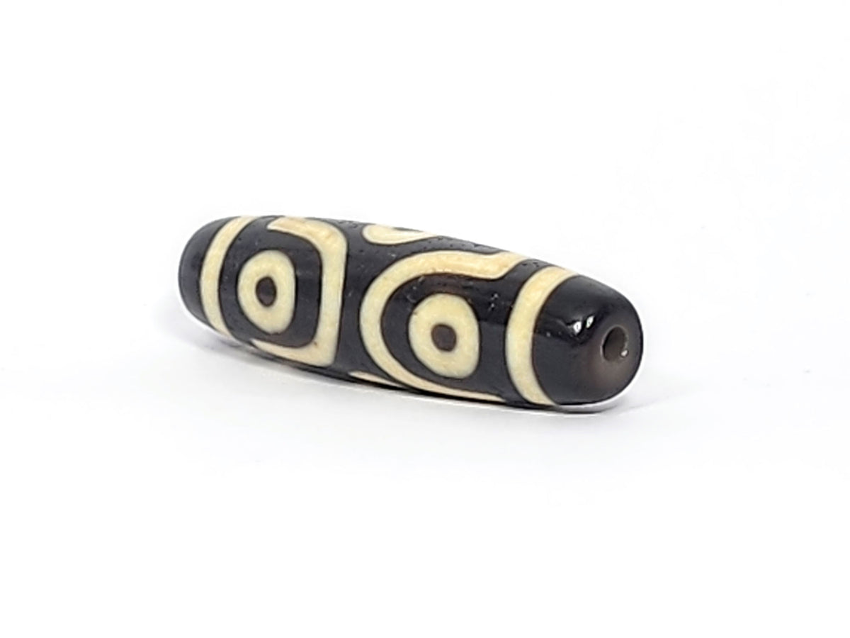 Opposite end cap of antique six eye dzi At-042925-6E2, pitch-black agate tip, drill hole, C-ring eyes and scroll motif visible on body, 41.4mm × 11.4mm, unretouched photography