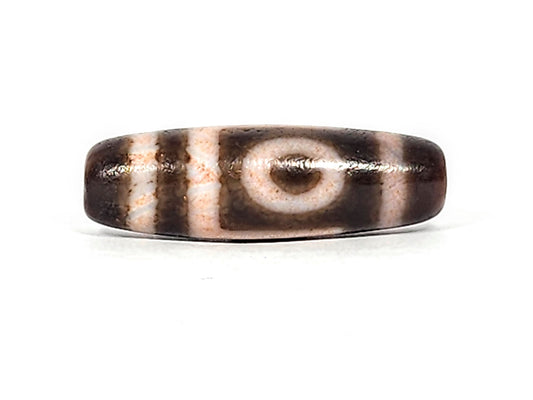 Three-quarter view of antique two eye dzi At-092724-2EBS, dark brown end cap with drill hole, one eye visible, warm dark brown torpedo body, 41.0mm × 13.0mm, unretouched