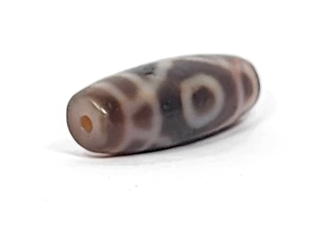 Antique two-eye dzi bead, dark agate, white eye motifs, bloodspots, aged patina, visible drill hole, oval barrel shape