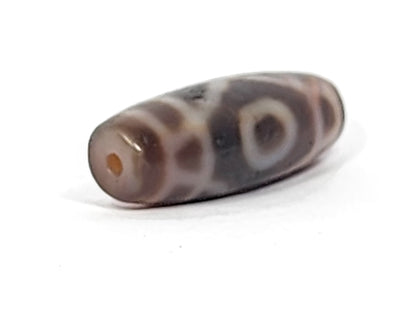 Antique two-eye dzi bead, dark agate, white eye motifs, bloodspots, aged patina, visible drill hole, oval barrel shape